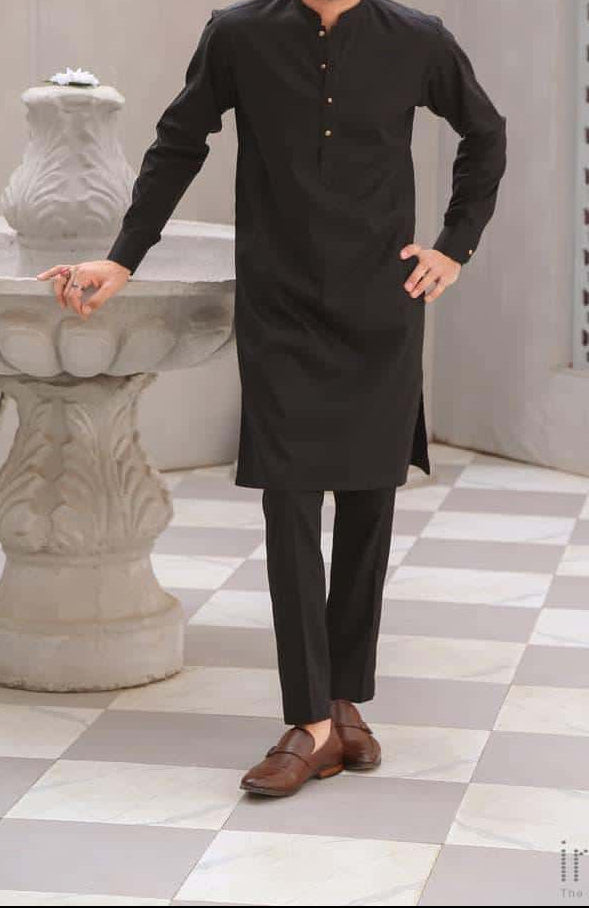 Man wearing a black kurta standing in a decorative indoor setting with checkered floor and architectural elements.
