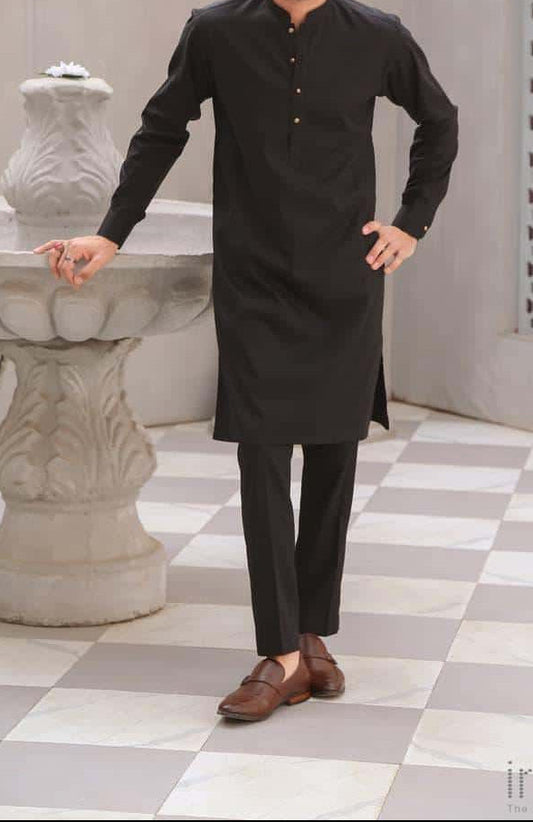 Man wearing a black kurta standing in a decorative indoor setting with checkered floor and architectural elements.