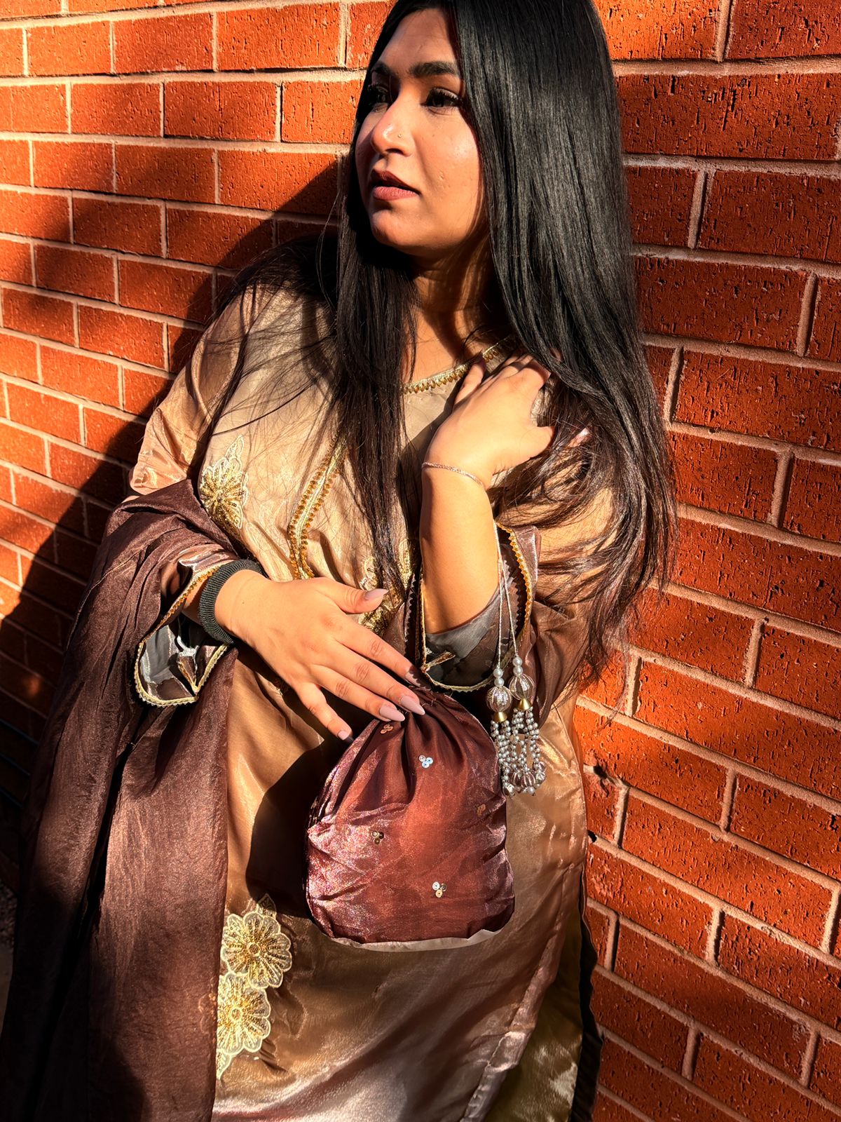 Woman in traditional attire holding a baguette against a brick wall